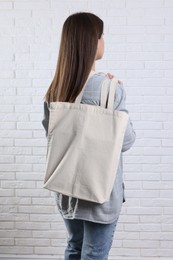 Woman with blank shopper bag near white brick wall, back view. Mockup for design