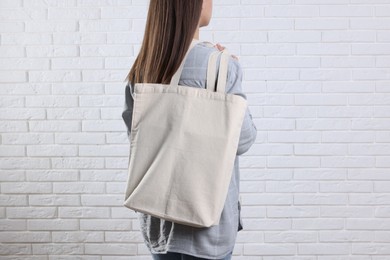 Photo of Woman with blank shopper bag near white brick wall, back view. Mockup for design