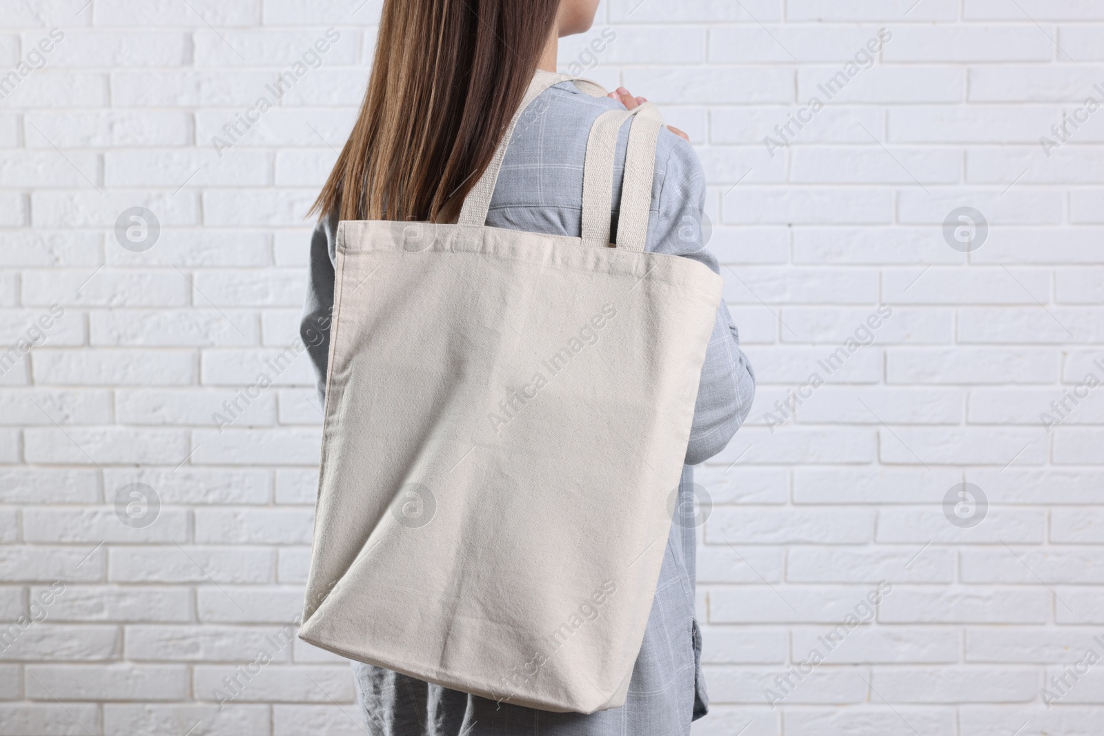 Photo of Woman with blank shopper bag near white brick wall, back view. Mockup for design