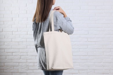 Photo of Woman with blank shopper bag near white brick wall, back view. Mockup for design