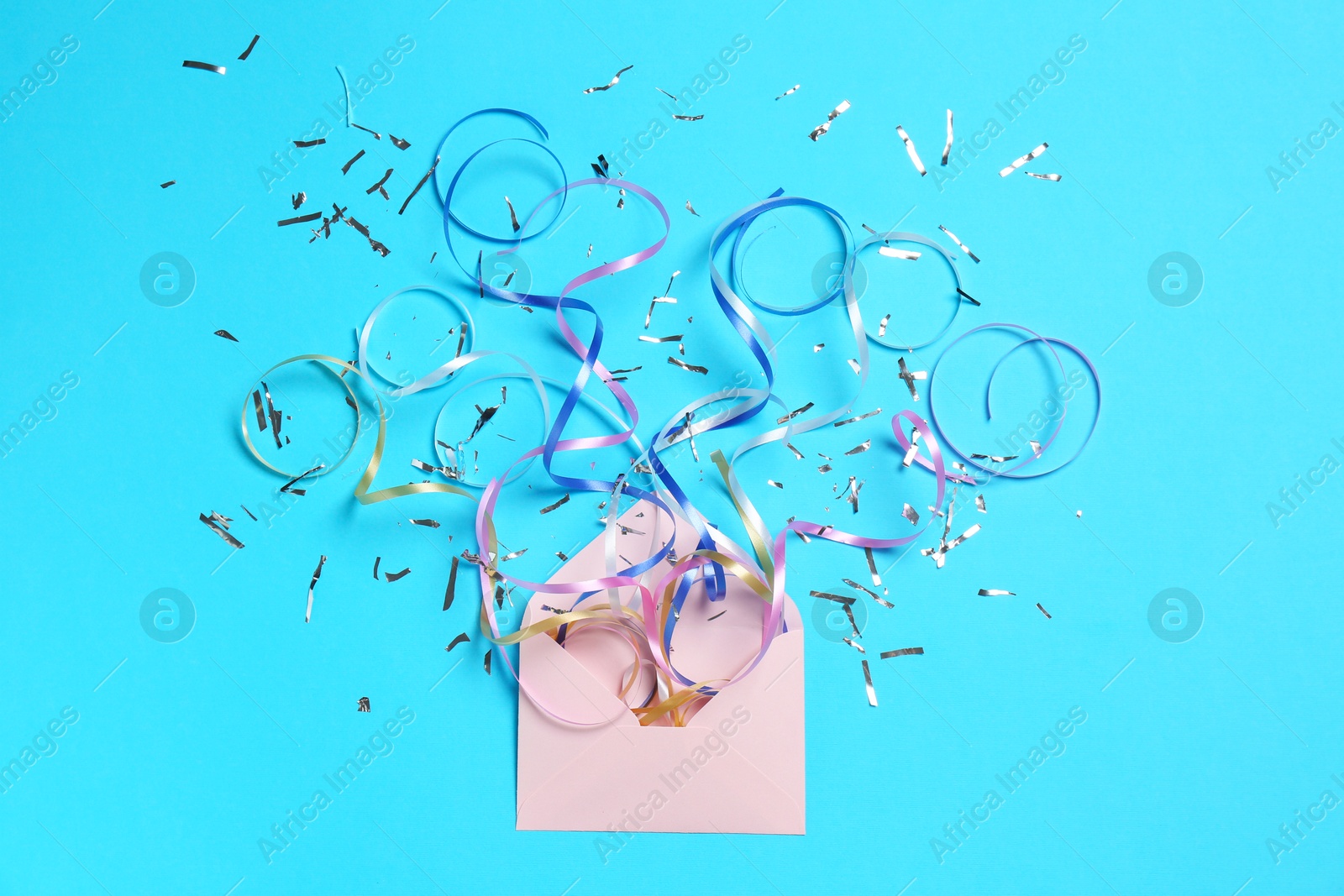 Photo of Shiny confetti and party streamers flying out of envelope on light blue background, flat lay