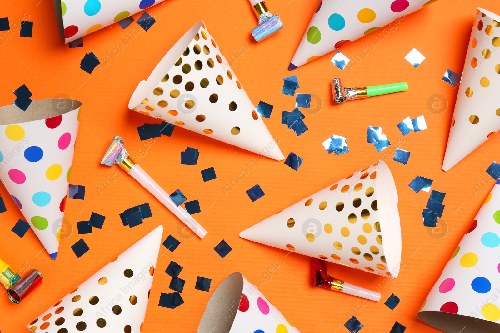 Photo of Shiny confetti, blowers and party hats on orange background, flat lay