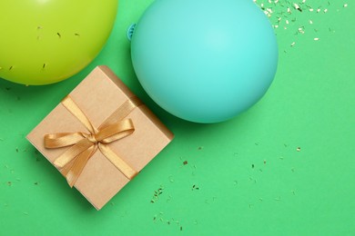 Photo of Gift box, balloons and shiny confetti on green background, flat lay