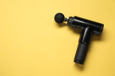 Photo of One black percussive massager on yellow background, top view. Space for text