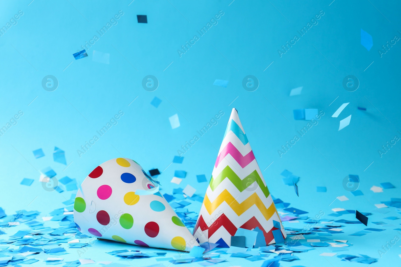 Photo of Beautiful confetti falling on party hats against light blue background