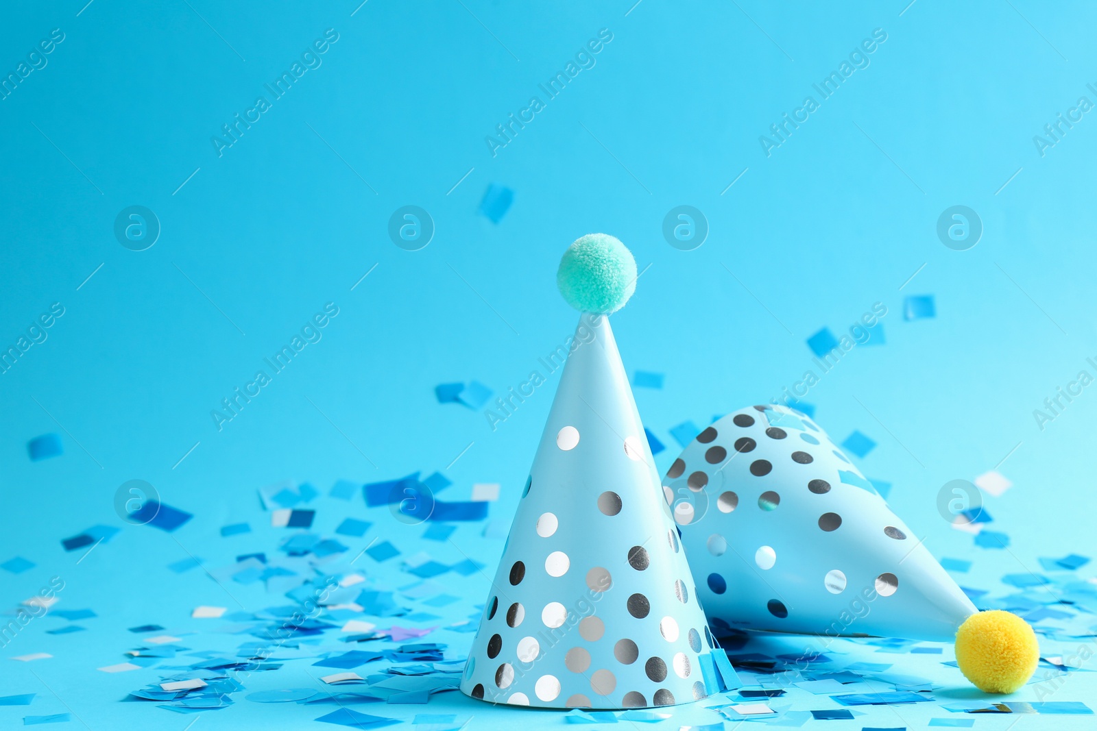 Photo of Beautiful confetti and party hats on light blue background, closeup. Space for text