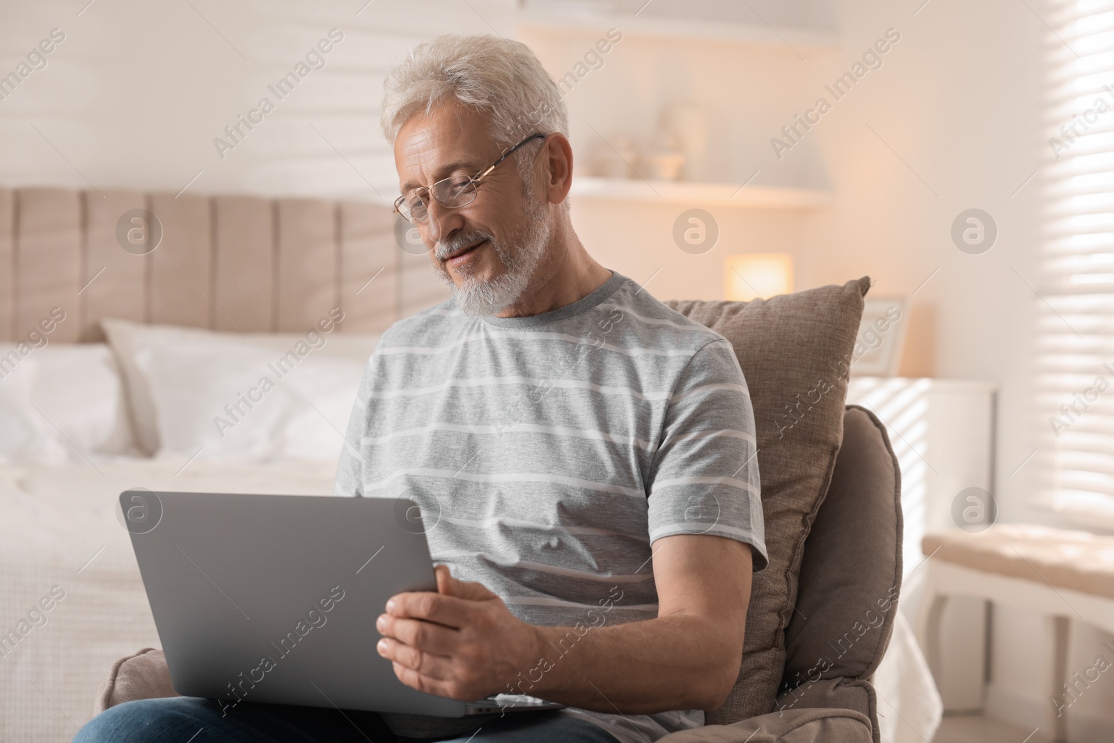 Photo of Senior man using laptop on armchair at home