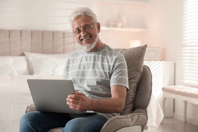 Photo of Happy senior man using laptop on armchair at home