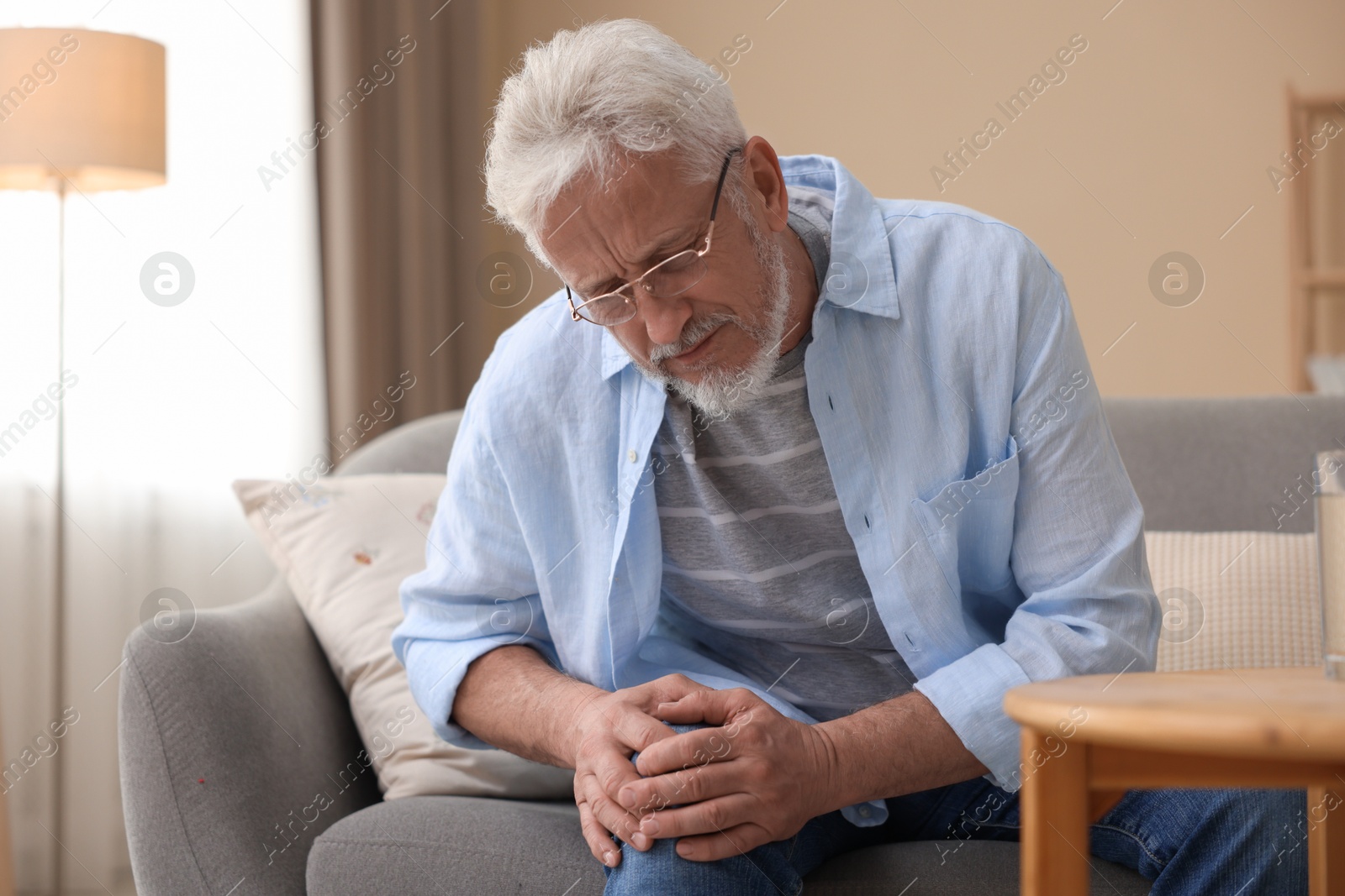 Photo of Senior man suffering from pain in knee at home