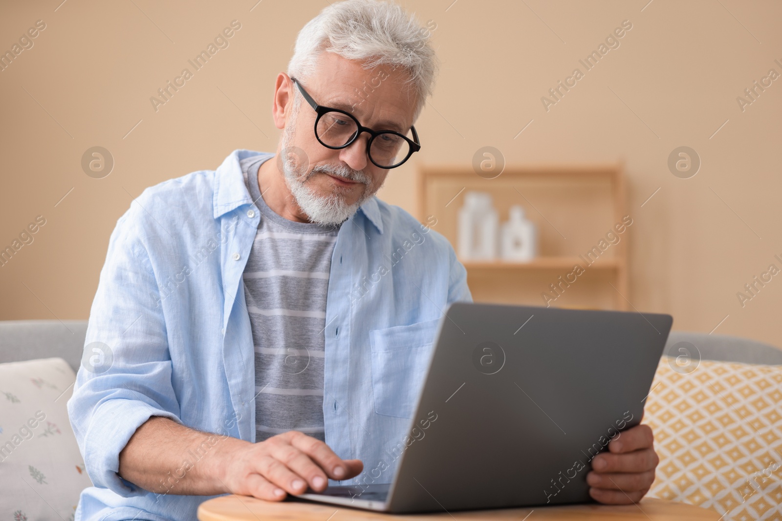 Photo of Senior man using laptop at wooden table indoors