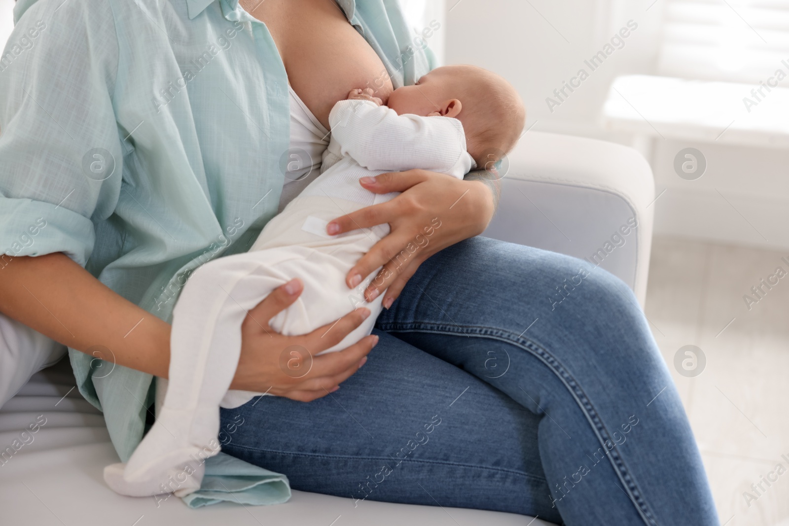 Photo of Mother breastfeeding her little baby on sofa at home, closeup