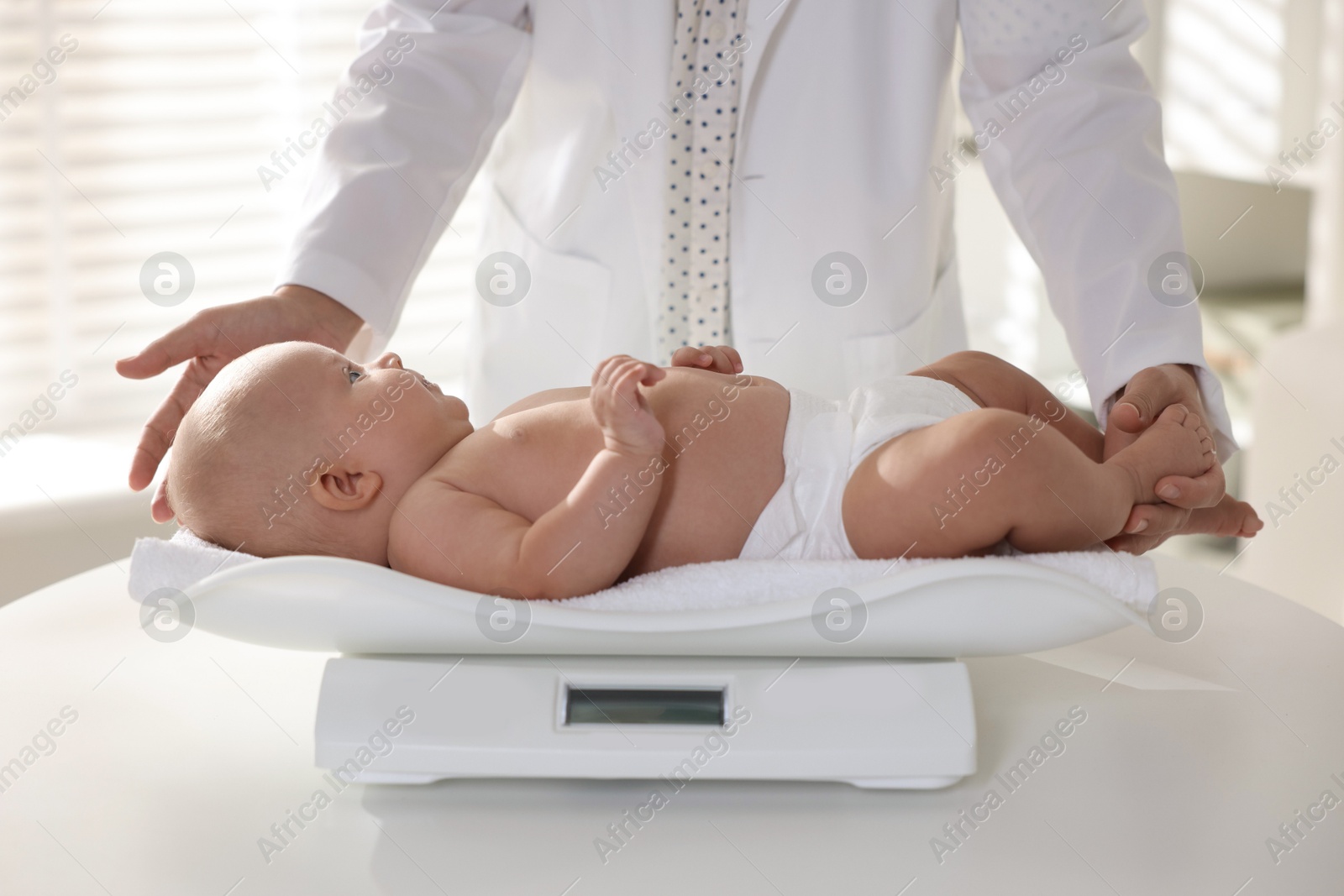 Photo of Pediatrician weighting little child in clinic, closeup. Checking baby's health