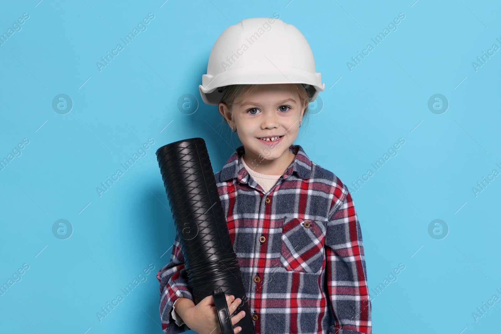 Photo of Little girl with blueprint tube pretending to be architect on light blue background. Dreaming of future profession