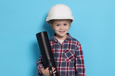 Photo of Little girl with blueprint tube pretending to be architect on light blue background. Dreaming of future profession