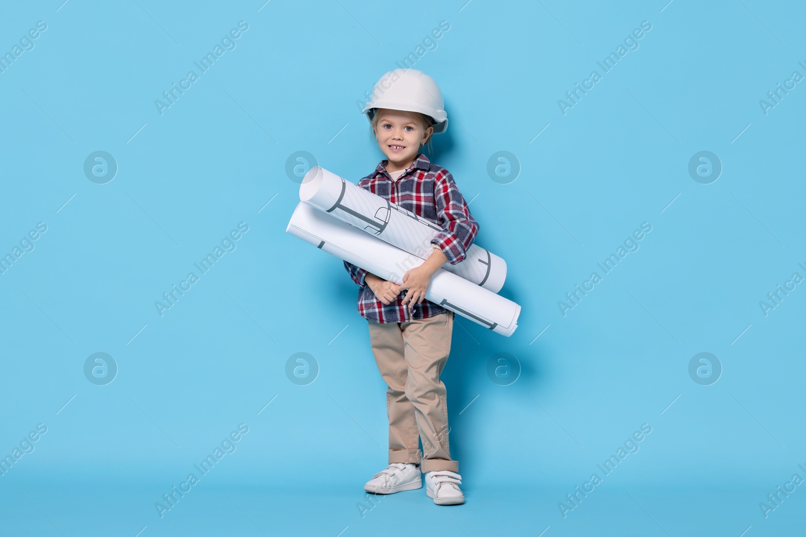 Photo of Little girl with house plan pretending to be architect on light blue background. Dreaming of future profession