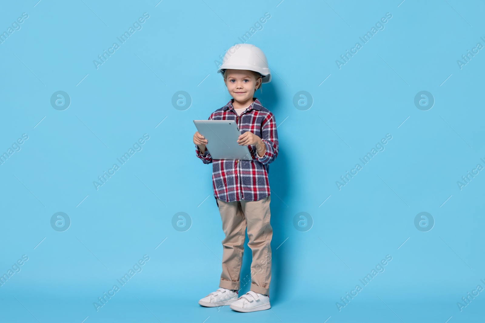 Photo of Little girl with tablet pretending to be architect on light blue background. Dreaming of future profession