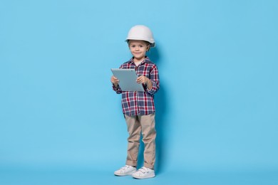 Little girl with tablet pretending to be architect on light blue background. Dreaming of future profession