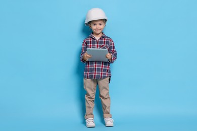 Photo of Little girl with tablet pretending to be architect on light blue background. Dreaming of future profession