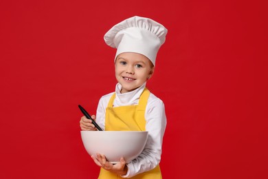 Photo of Little girl with bowl and spoon pretending to be chef on red background. Dreaming of future profession