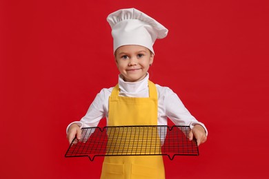 Little girl with cooling rack pretending to be chef on red background. Dreaming of future profession