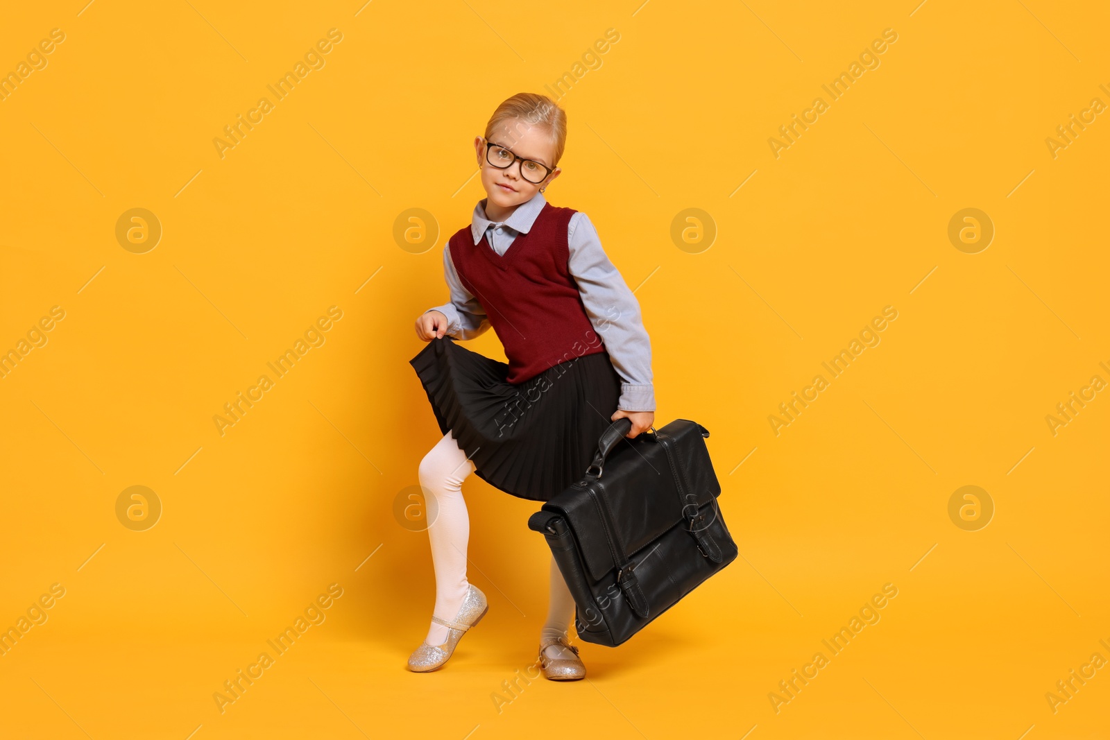 Photo of Little girl with glasses and briefcase on orange background. Dreaming of future profession