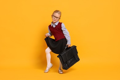 Little girl with glasses and briefcase on orange background. Dreaming of future profession