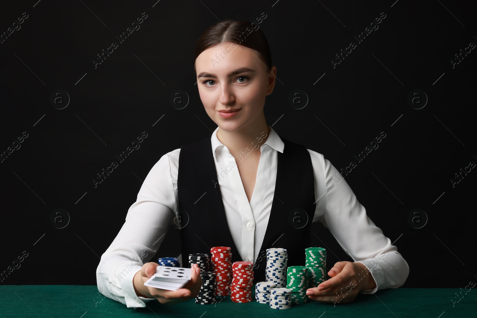 Photo of Professional croupier with casino chips and playing cards at gambling table on black background