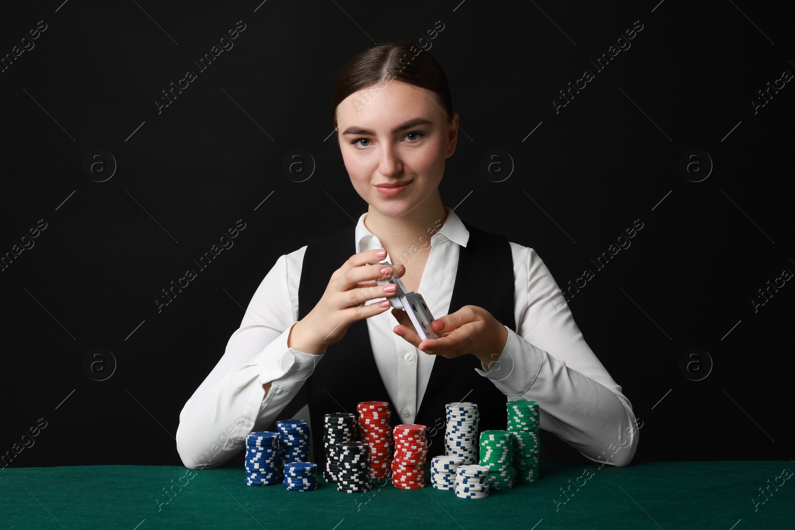 Photo of Professional croupier with casino chips and playing cards at gambling table on black background