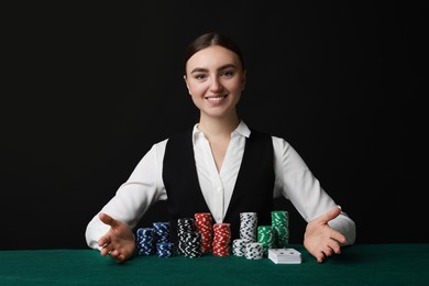 Photo of Professional croupier with casino chips and playing cards at gambling table on black background