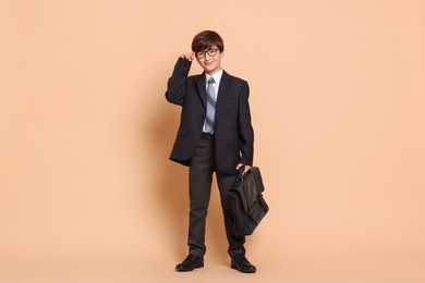 Photo of Boy in suit pretending to be businessman on beige background. Dreaming of future profession