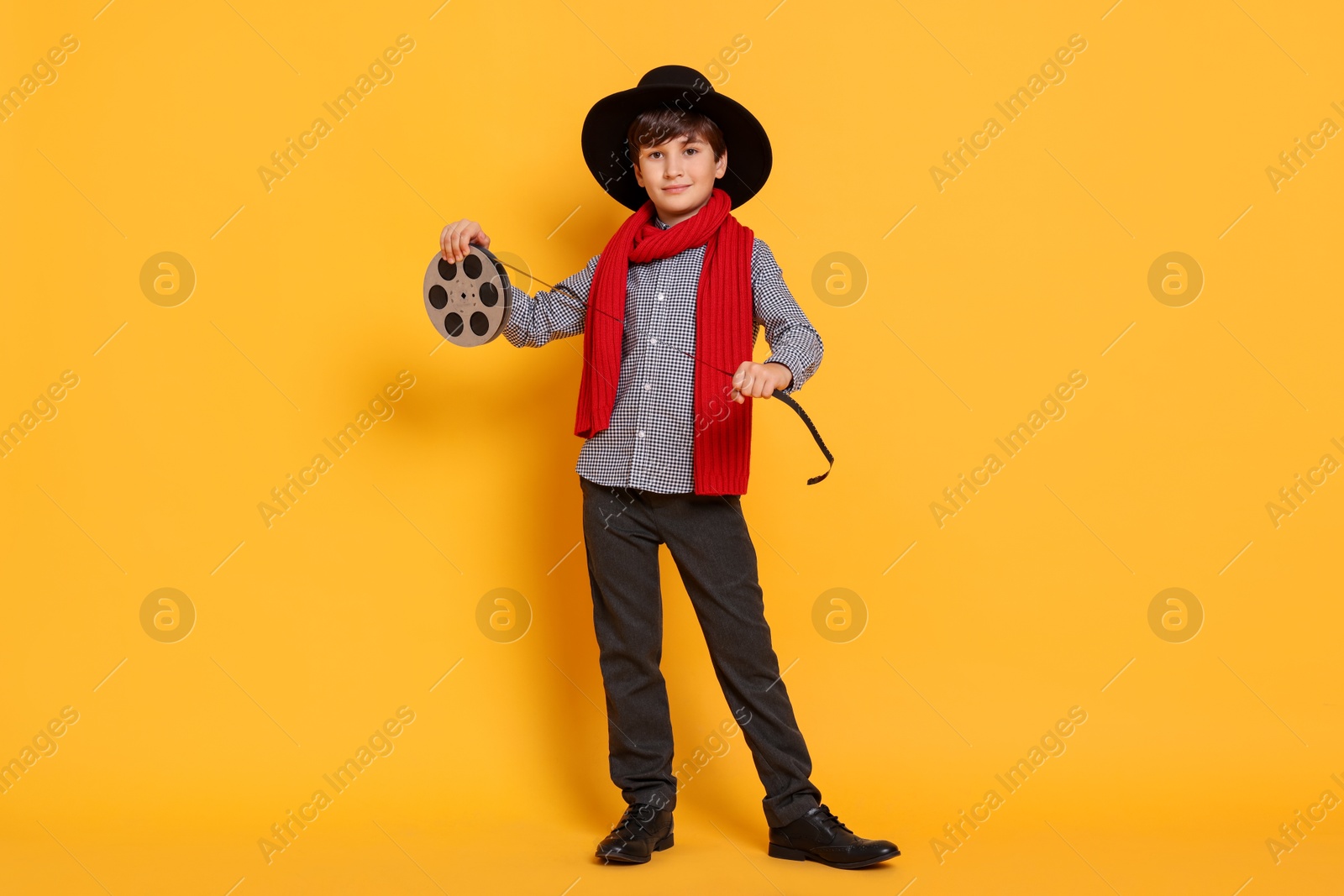 Photo of Boy with film reel pretending to be movie director on orange background. Dreaming of future profession