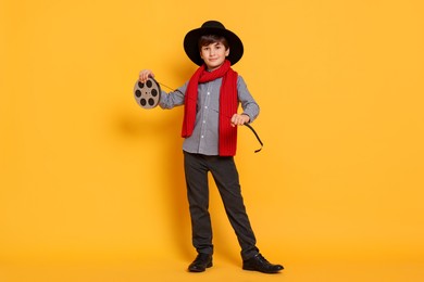 Photo of Boy with film reel pretending to be movie director on orange background. Dreaming of future profession