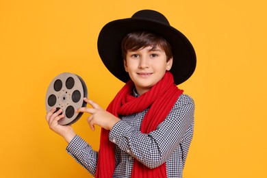 Boy with film reel pretending to be movie director on orange background. Dreaming of future profession