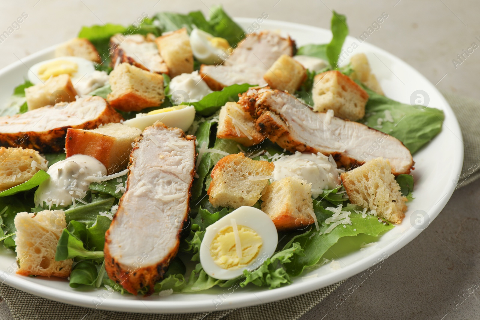 Photo of Tasty Caesar salad with chicken on light grey table, closeup