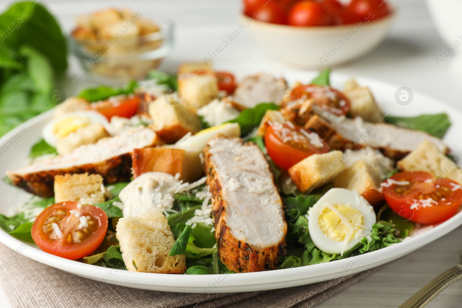 Photo of Tasty Caesar salad with chicken and tomatoes on white wooden table, closeup