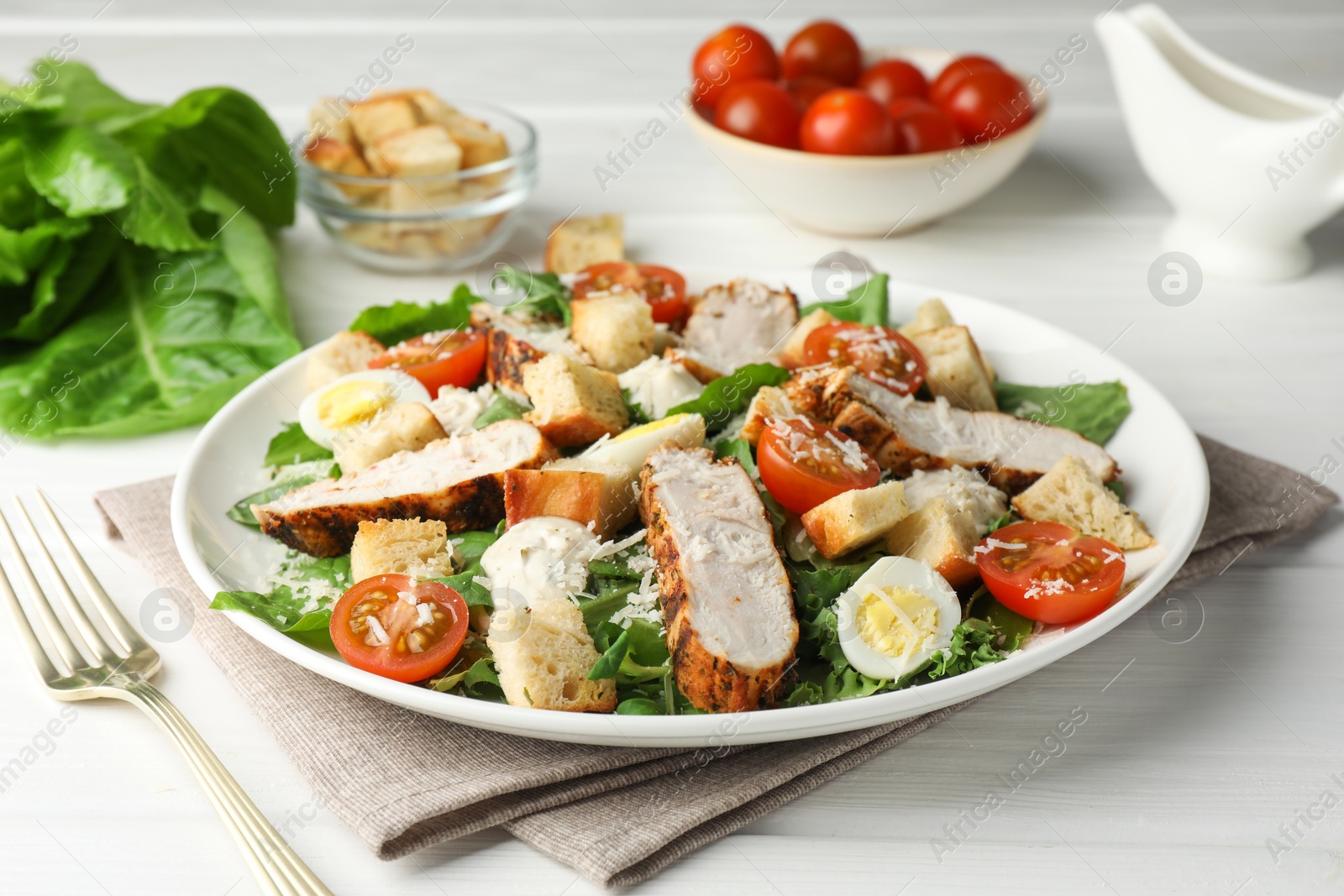 Photo of Tasty Caesar salad with chicken and tomatoes on white wooden table