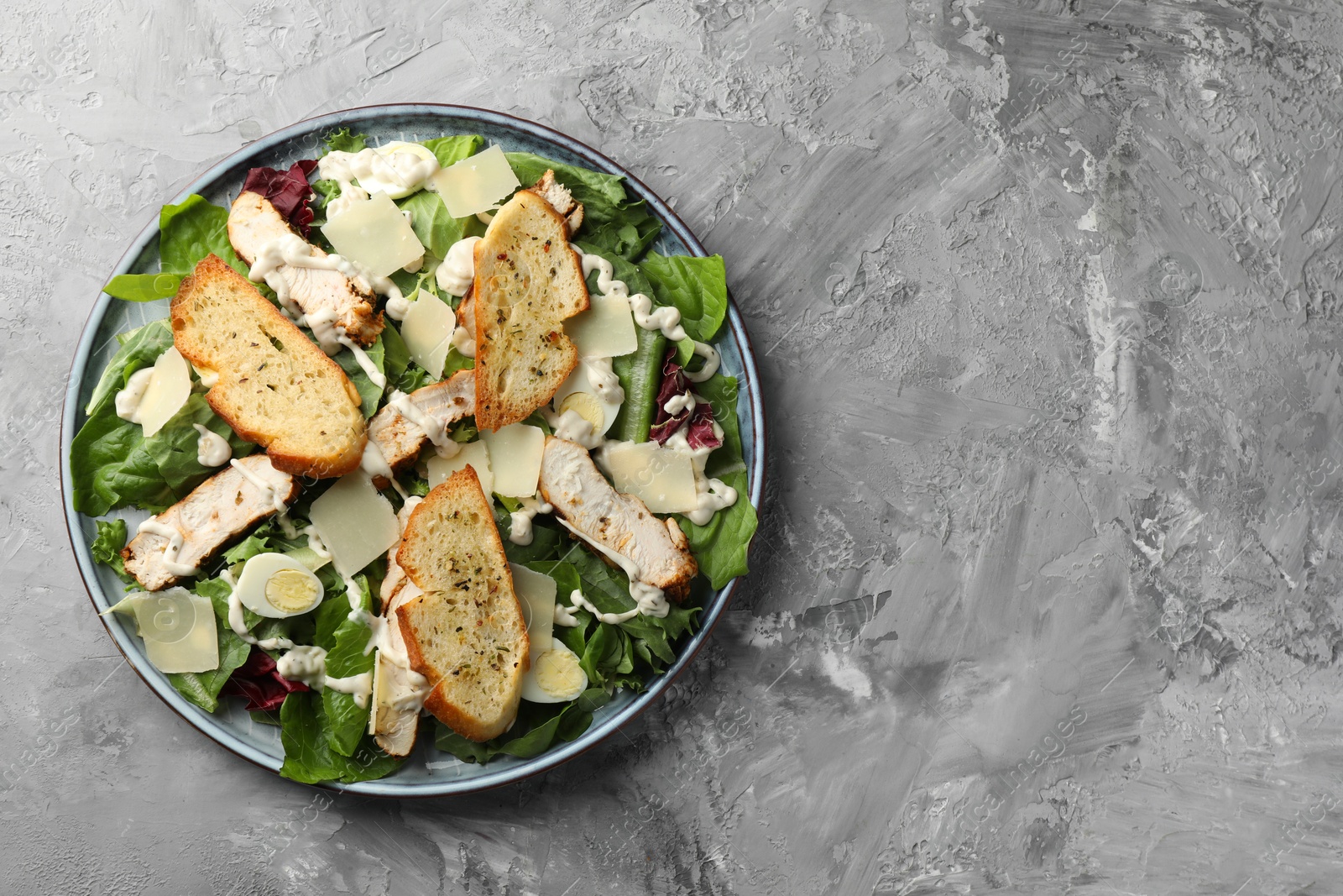 Photo of Tasty Caesar salad with chicken on gray textured table, top view. Space for text