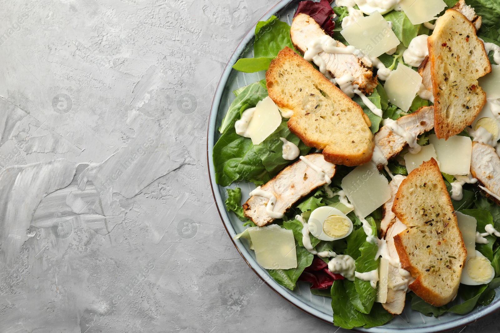 Photo of Tasty Caesar salad with chicken on gray textured table, top view. Space for text