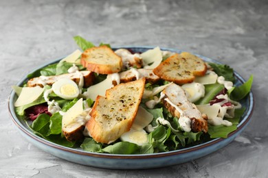 Photo of Tasty Caesar salad with chicken on gray textured table, closeup