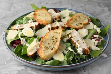 Photo of Tasty Caesar salad with chicken on gray textured table, closeup