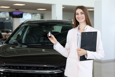 Photo of Happy saleswoman holding key near new black car in salon