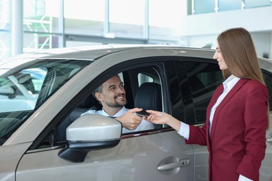 Photo of Happy saleswoman and client inside new silver car in salon