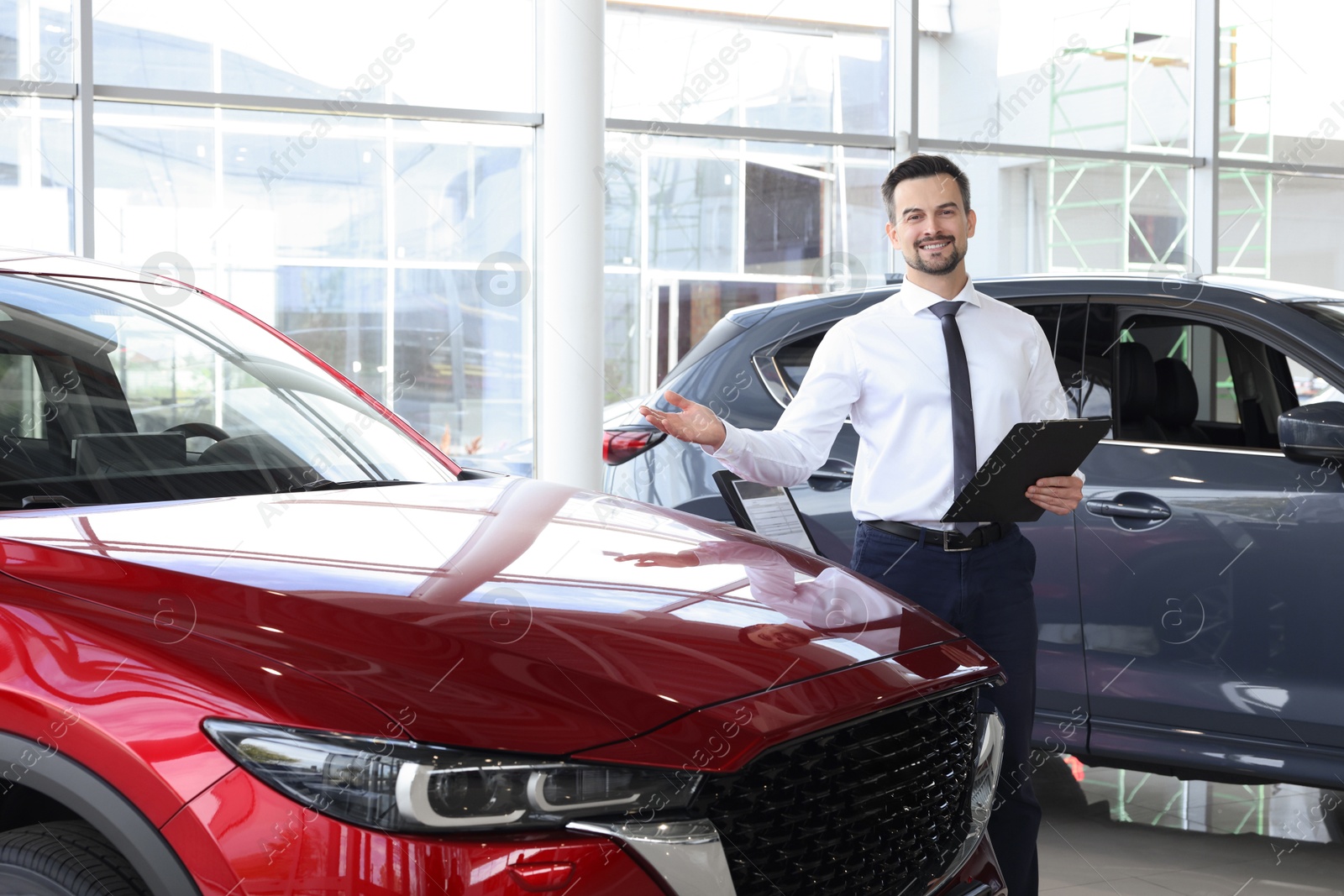 Photo of Happy salesman near new red car in salon