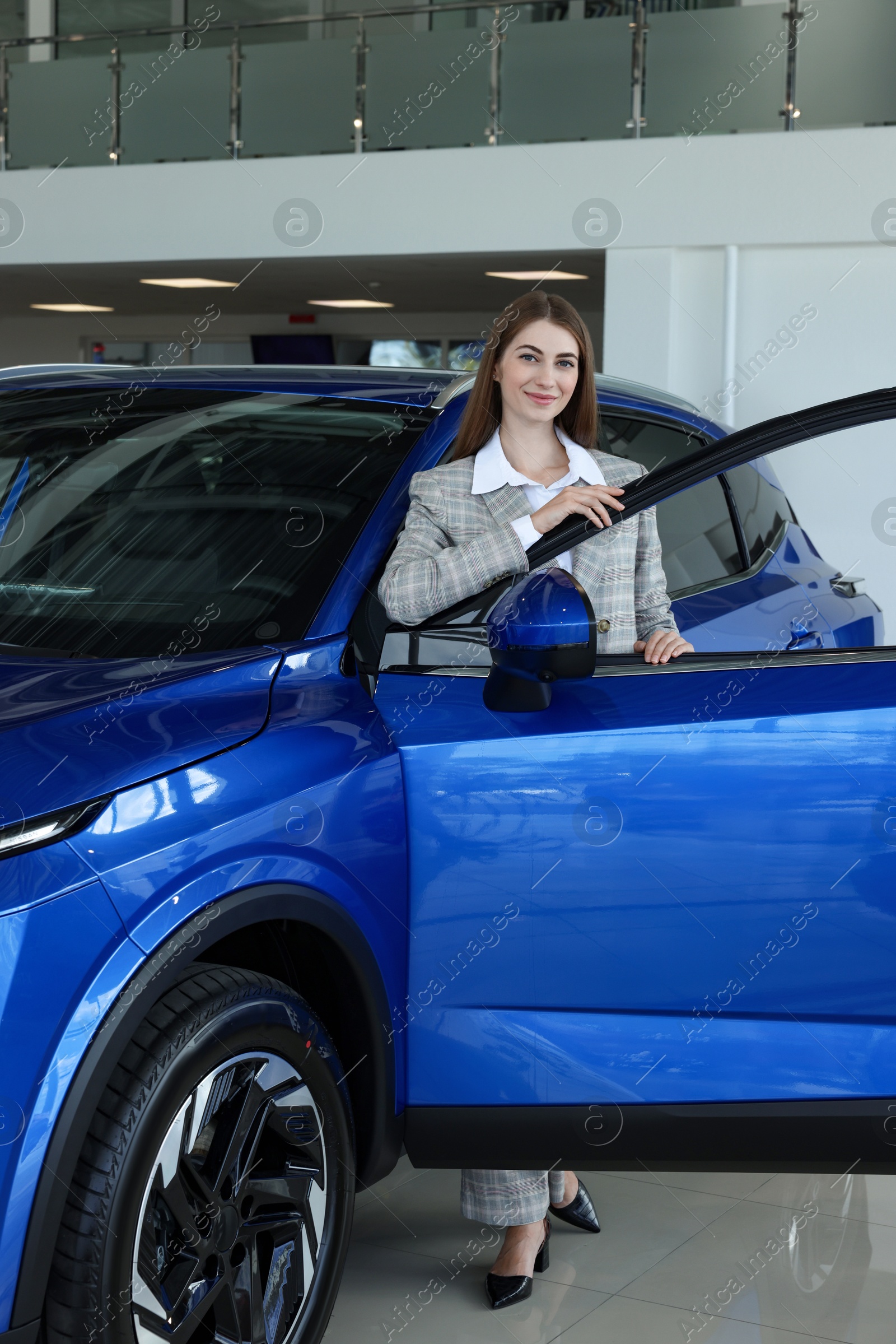 Photo of Young woman near new blue car in salon