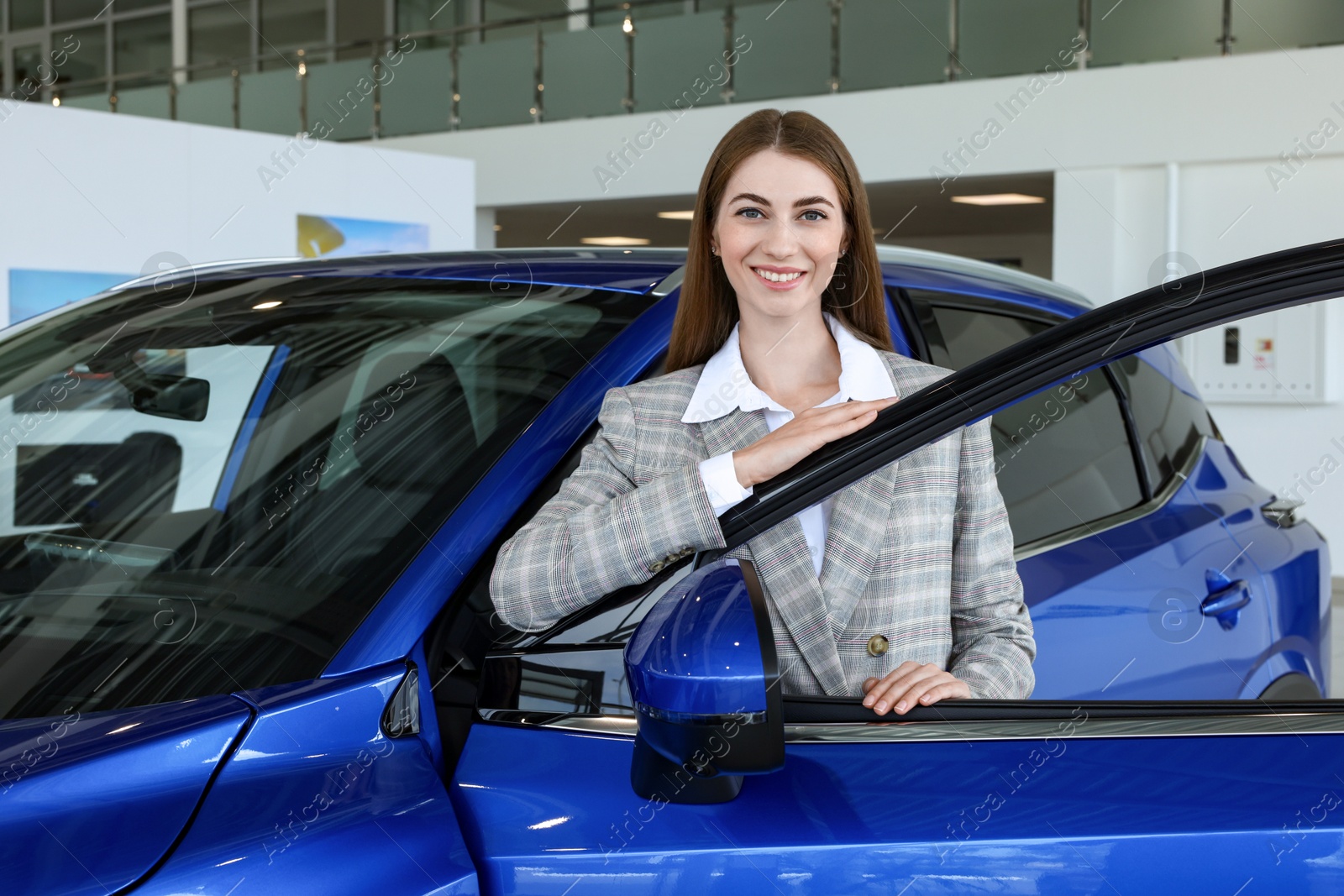 Photo of Young woman near new blue car in salon