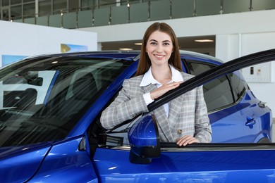 Young woman near new blue car in salon