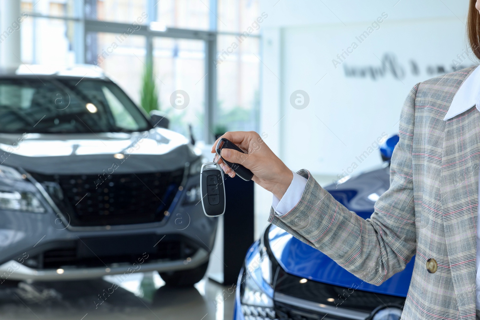 Photo of Saleswoman holding key near new car in salon, closeup