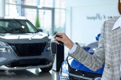 Saleswoman holding key near new car in salon, closeup