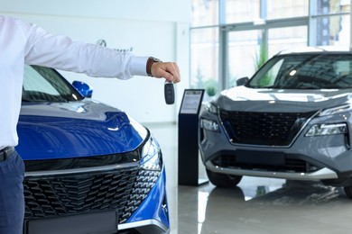 Photo of Salesman holding key near new car in salon, closeup