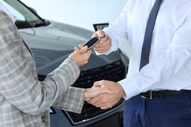 Salesman giving key to client near new car in salon, closeup